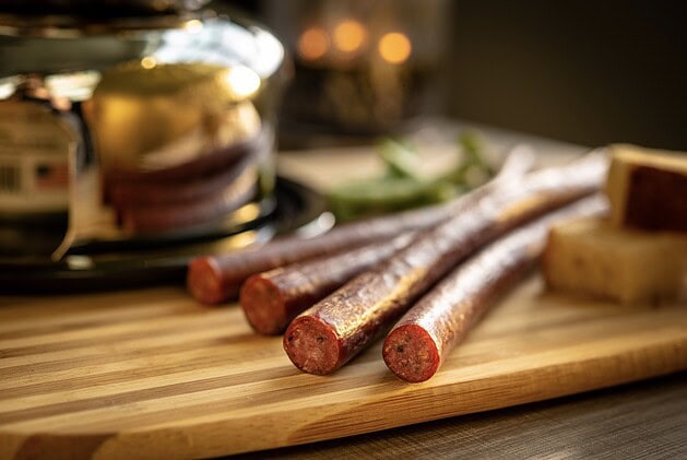Three cured snack sticks on a bamboo cutting board