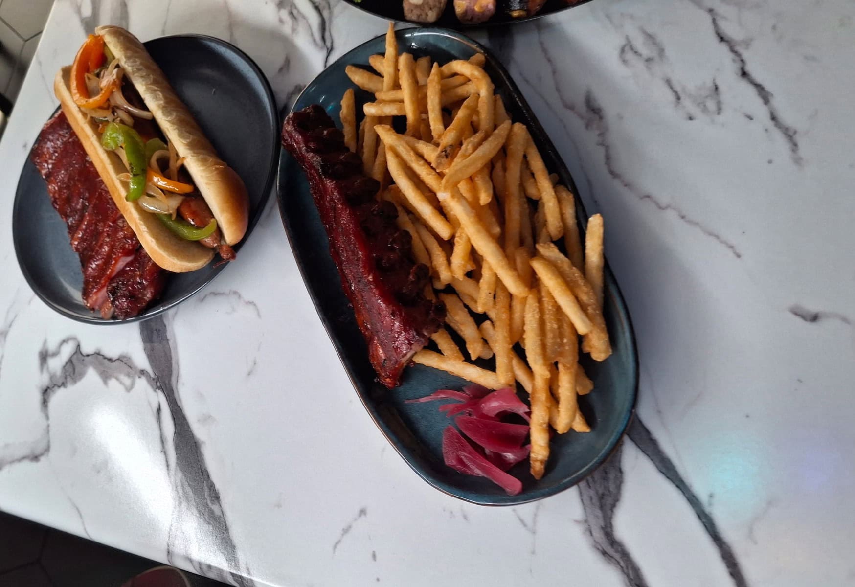 BBQ ribs with fries and pickles on a black plate at Homestead Meat Company.