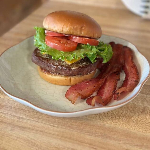 Juicy beef burger with lettuce, tomato, and bacon on a bun.