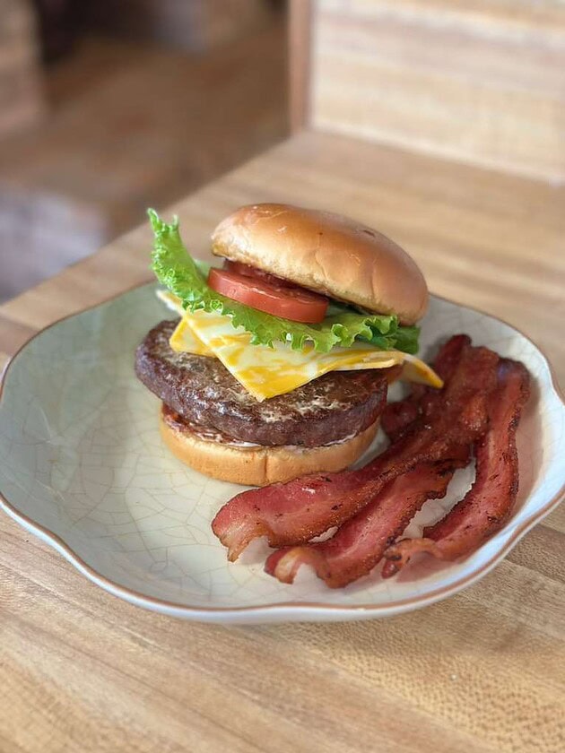 Juicy homemade burger with lettuce, tomato, cheese, and bacon on a plate.